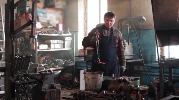 Manusia pandai besi mengeluarkan detail logam panas dari tungku dan mendinginkan diri dalam seember air — Stok Video