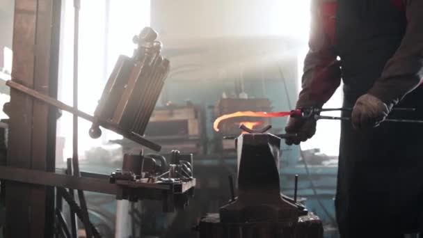 Homem ferreiro tira um pedaço de metal de um forno - coloca-o na forma na bigorna e começa a bater o detalhe com um martelo — Vídeo de Stock