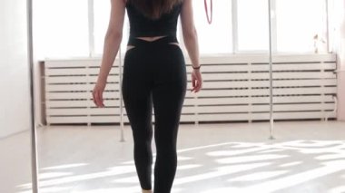 Genç bir jimnastik kadın tavanın altındaki ringe doğru yürür ve kameraya bakar.