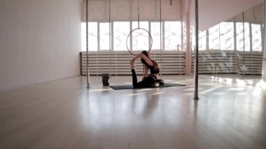 Genç bir kadın, beyaz stüdyoda yoga minderinde esniyor ve egzersiz yapıyor.