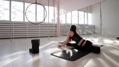 Beyaz bir stüdyoda yoga minderinin üzerinde uzanan genç bir jimnastik kadını.