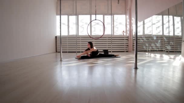 En ung kvinna som sitter i en spricka på golvet och stretchar — Stockvideo