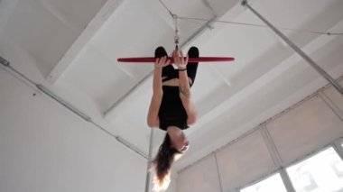 Tavanın altında asılı duran spor ringinde baş aşağı dönen genç bir jimnastik kadını.