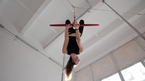Una giovane donna ginnica appesa e girando a testa in giù sul ring sportivo appeso sotto il soffitto — Video Stock