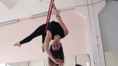 Genç bir kadın jimnastikçi akrobatik ringde baş aşağı duruyor.