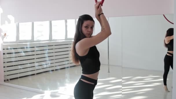 Молода жінка-гімнастка тримається за акробатичне кільце і дивиться в камеру в студії — стокове відео