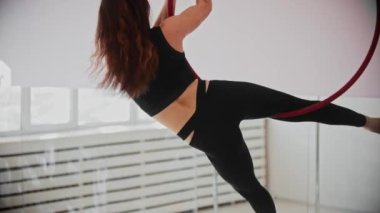 Tavanın altında asılı bir yüzükle akrobatik hareketler yapan genç bir plastik kadın.