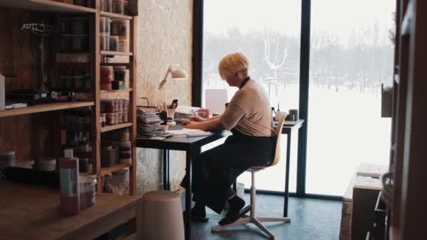 Una anciana artista trabajando junto a la mesa en el taller — Vídeos de Stock