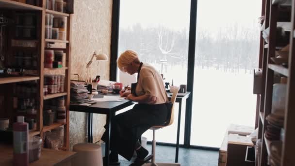 ワークショップのテーブルで働く年配の女性アーティスト-スケッチを描く — ストック動画