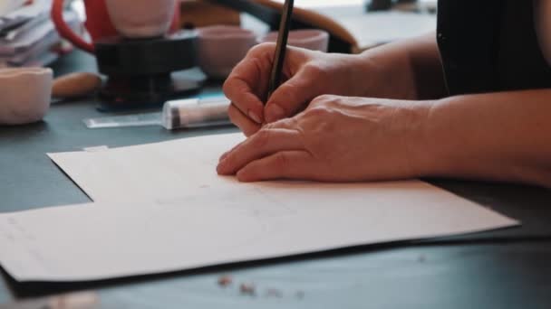 Una mujer anciana diseñadora dibujando en el papel usando una regla — Vídeos de Stock