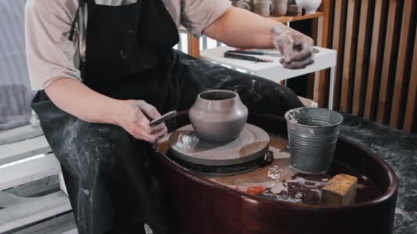 Aardewerk - een oudere vrouw die de kleipot met haar handen en houten kam vormgeeft — Stockvideo