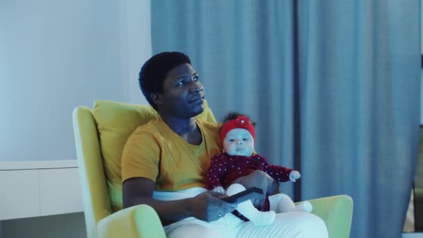 Padre nero seduto con il suo bambino e guarda la TV - fratelli maggiori viene da lui e mostra i loro compiti — Video Stock