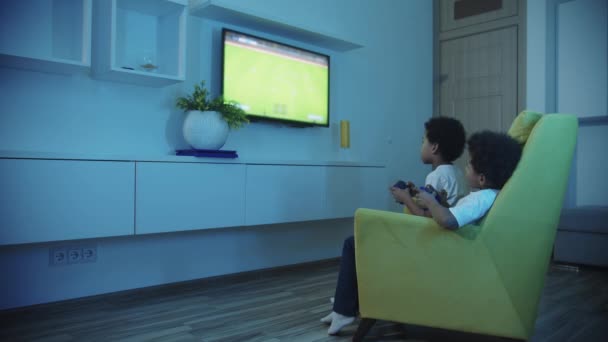 Two little black boys brothers playing football game on TV using joysticks — Wideo stockowe