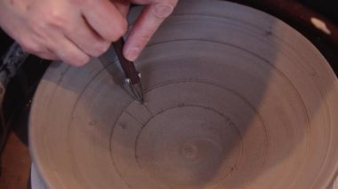 Bir kadın kil levhaya bir alet kullanarak bir desen kazıyor.