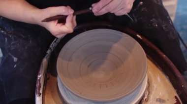 Bir kadın kil tabağa bir alet kullanarak oyuk kazıyor.