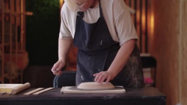 Yaşlı bir kadın kilden bir parça kesiyor.