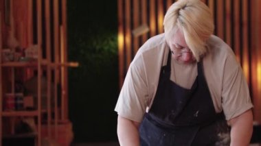 Yaşlı bir kadın bir parça çamuru merdaneyle düzleştiriyor.