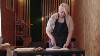 Kısa saçlı yaşlı bir kadın tahtaya bir parça kil atar.