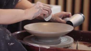 Bir kadın çömlek tekerindeki kil tabağı saç kurutma makinesiyle ısıtıyor ve içerideki kilden fazla kilden kurtuluyor.