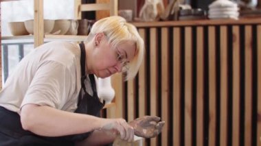 Yaşlı bir kadın çömlek tekerindeki ıslak kil tabakta sünger kullanıyor.