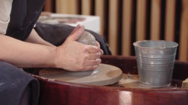 Yaşlı bir kadının elleri çömlek çarkına ıslak bir kil parçası çekiyor.