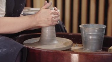 Yaşlı bir kadının elleri çömlek çarkında ıslak bir kil parçasını yukarı aşağı çeker.