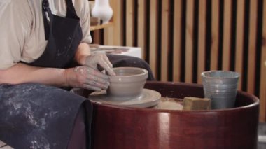 Yaşlı bir kadın çömlek çarkında kilden bir parça şekillendiriyor.