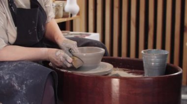 Yaşlı bir kadın ıslak sünger kullanarak çömlek çarkında kilden bir parça şekillendiriyor.