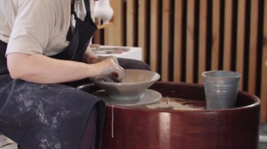 Yaşlı bir kadın, hareket halindeki çömlek çarkında kilden çorba tabağını şekillendiriyor.