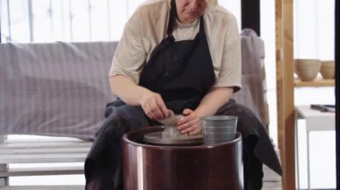 Yaşlı bir kadın atölyede kilini ıslatıyor.