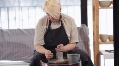 Yaşlı bir kadın atölyedeki kil parçasını yumuşatıyor.