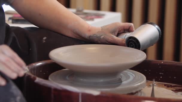 A woman heating a clay plate on the wheel using hairdryer — Stockvideo