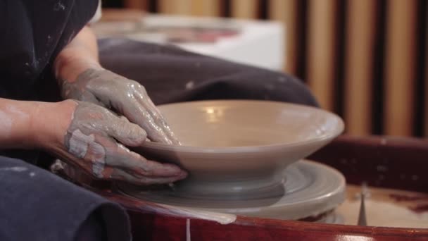 Χέρια ηλικιωμένης γυναίκας που φτιάχνει πήλινη πλάκα στον κεραμικό τροχό — Αρχείο Βίντεο
