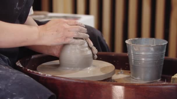 Mãos de mulher idosa molhando um piolho de barro e amassando-o na roda de cerâmica em movimento — Vídeo de Stock