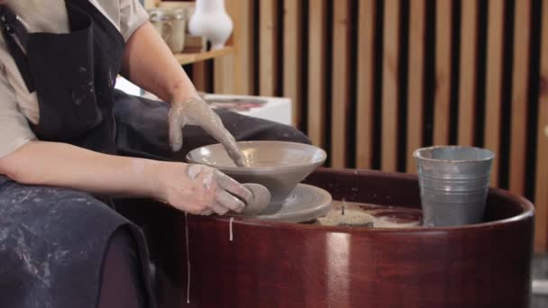 Egy idős nő, aki egy tányért formál agyagból a kerámia keréken. — Stock videók
