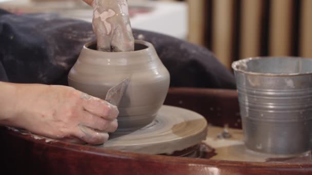 Eine ältere Frau formt mit einem flachen Werkzeug und ihren Händen einen Tontopf auf einer beweglichen Töpferscheibe — Stockvideo