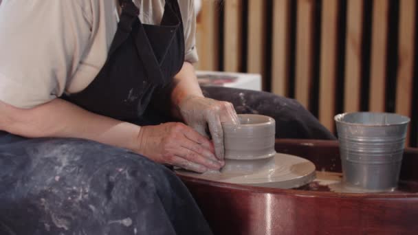 Een oudere vrouw vormt een hoge klei pot op bewegend aardewerk wiel in de werkplaats — Stockvideo