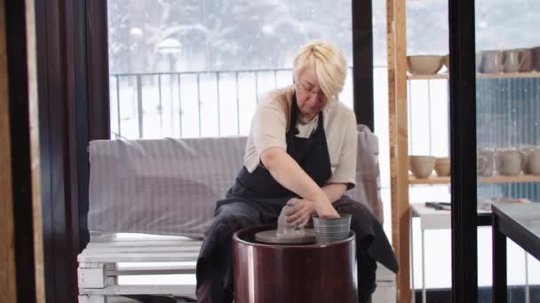 An elderly woman softening the piece of clay in the workshop using water and sponge — Vídeo de Stock