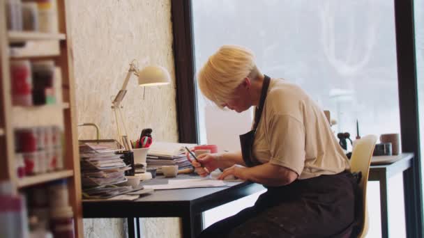 An elderly woman with short hair sketching design for a new clay item in the workshop — Stock Video