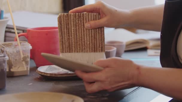 An elderly woman using a big brush to color new clay plate — Vídeo de Stock