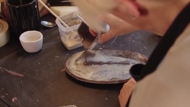 An elderly woman pouring brown color paint on the new clay plate — Video