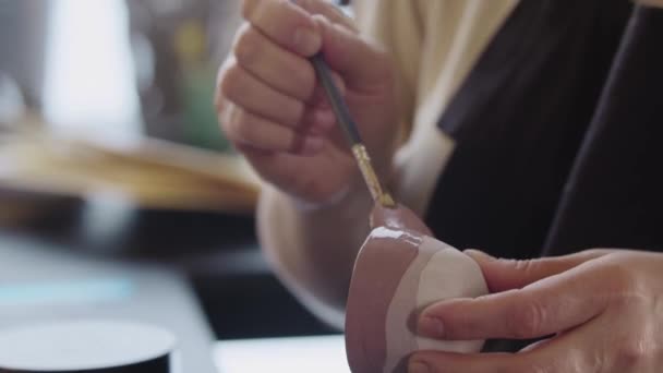 Hands of an elderly woman painting a little clay cup with dusty rose color — Vídeo de stock