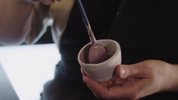 Hands of an old woman painting a little clay cup with dusty rose color — Stockvideo