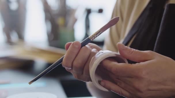 Hands of an elderly woman painting a little clay cup with dusty rose color using a brush — Stockvideo