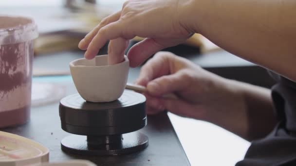Hands of an old woman puts a little clay cup on the rotating wheel — Stock Video