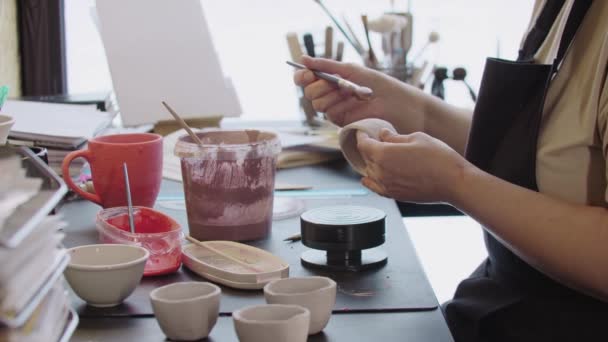 Manos de una anciana pintando una pequeña taza de barro con color rosa polvoriento — Vídeos de Stock