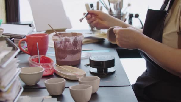 Стара жінка малює маленьку глиняну чашку з забрудненим рожевим кольором — стокове відео
