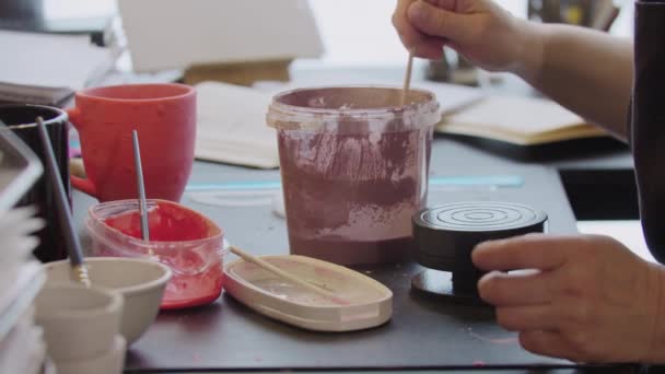 An elderly woman mixing dusty rose paint in the bucket with a brush — Stockvideo