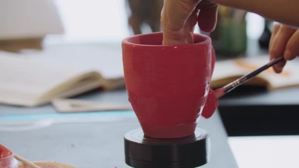 Hands of an old woman painting clay mug in red color — Stockvideo