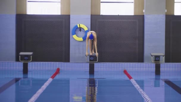 Młoda pływaczka opuszcza gogle i nurkuje w wodzie basenu. — Wideo stockowe
